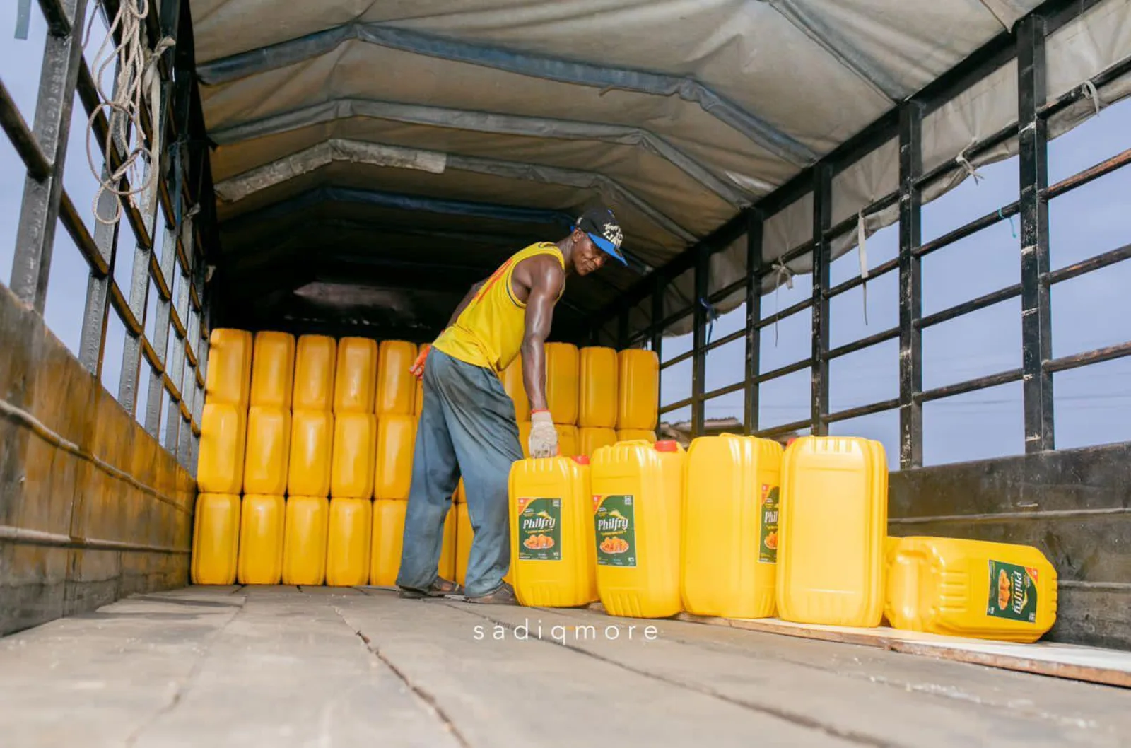 Worker loading yellow Philfry oil jerry cans onto a covered delivery truck